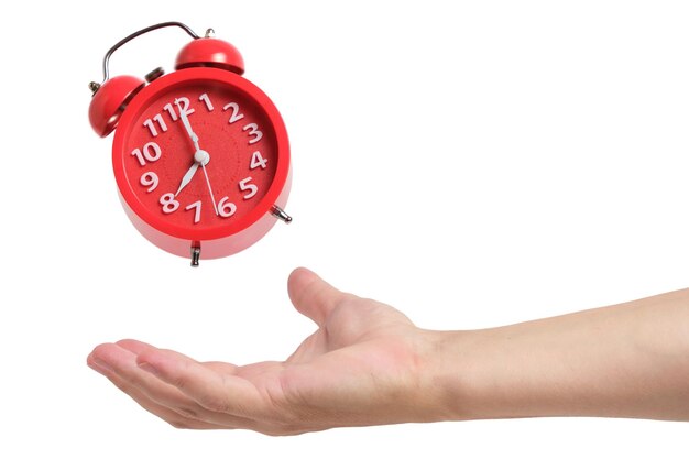 Ringing and levitating red alarm clock above hand on white background
