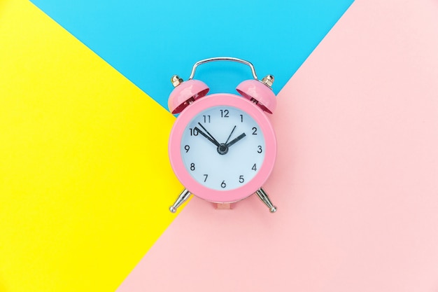 青黄色ピンクパステルカラフルな幾何学的な背景に分離されたリンギングツインベル古典的な目覚まし時計。休憩時間の人生の時間おはよう夜目を覚ましコンセプト。フラットレイアウトトップビューコピースペース。