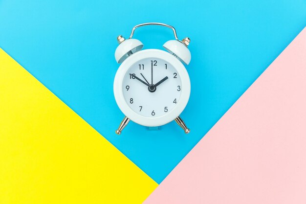 Ringing twin bell classic alarm clock isolated on blue yellow pink pastel colorful geometric background