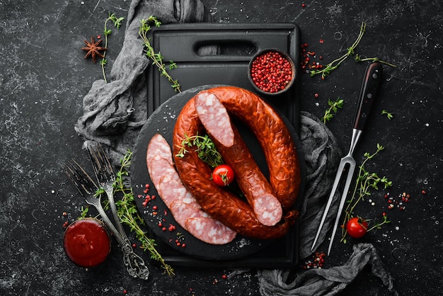 Rings of traditional smoked sausage in a country style composition on a black stone background Top view Free space for text