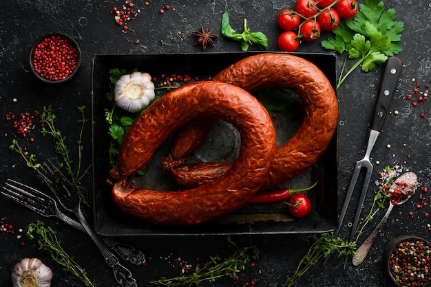 Rings of traditional smoked sausage in a country style composition on a black stone background Top view Free space for text