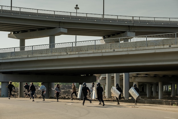 Riot police with shields running for young law-breakers under bridges to catch them and arrest