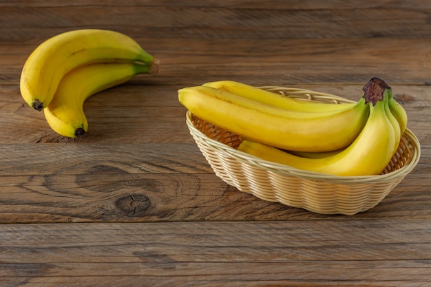 木製の背景に籐のバスケットでバナナの束をリッピングします。健康的な食事の概念。