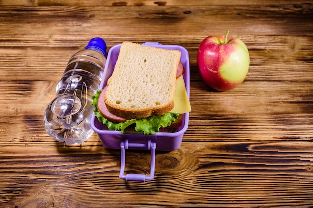 熟したリンゴのボトル入り飲料水と木製のテーブルにサンドイッチとランチボックス