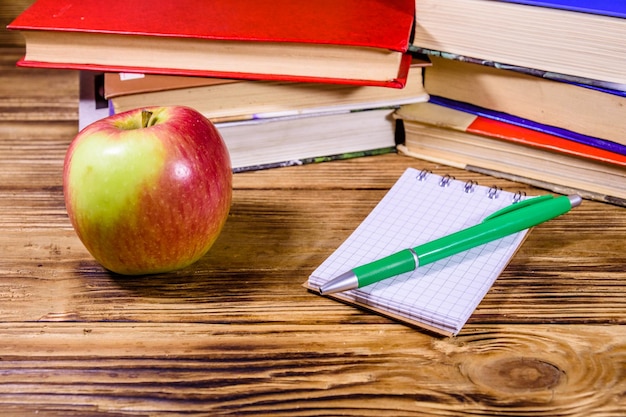 Фото Спелое яблоко открыло маленький блокнот и шариковую ручку на деревянном столе перед стопкой книг