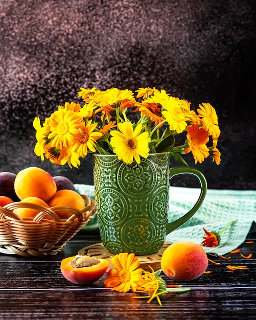 Ripe apricots in a basket and yellow calendula flowers in a vase