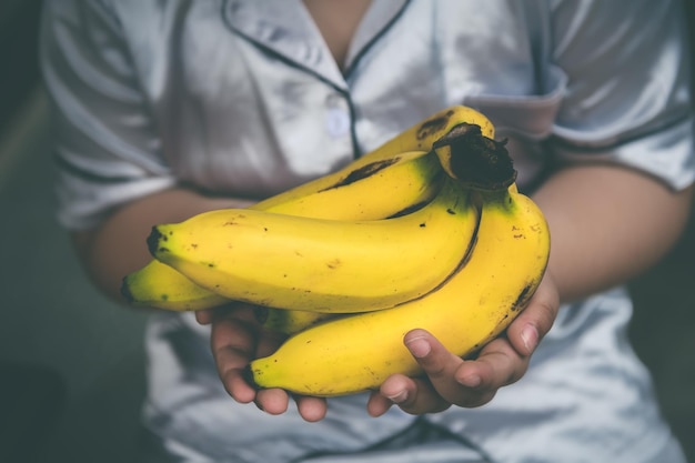 Foto banane mature in mano al bambino con luce naturale e toni grigi scuri