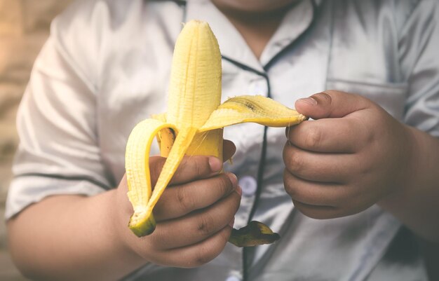 Foto banane mature in mano al bambino con luce naturale e toni grigi scuri