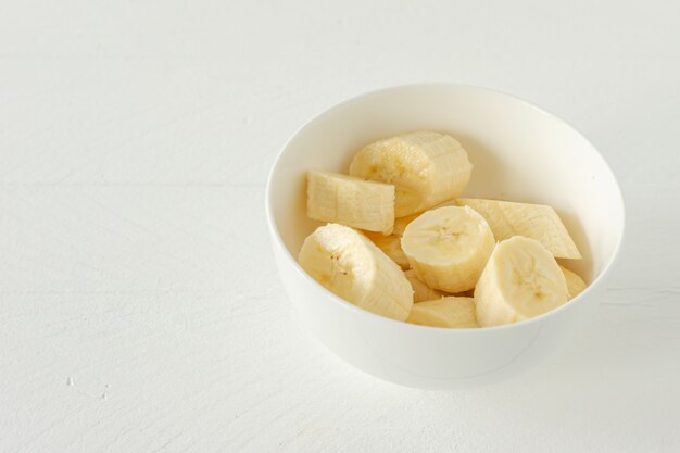 熟したバナナを白いボウルに切って食べます。健康的なスナックや朝食のコンセプト。