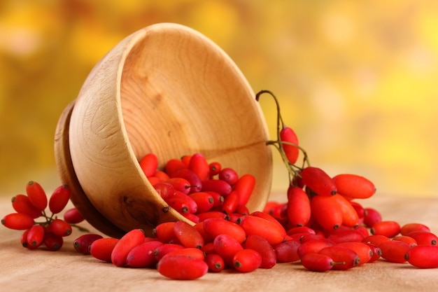 Image of ripe barberries in wooden bowl, on table, on yellow background