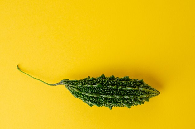 Photo ripe bitter gourd or momordica on yellow background with copy space.