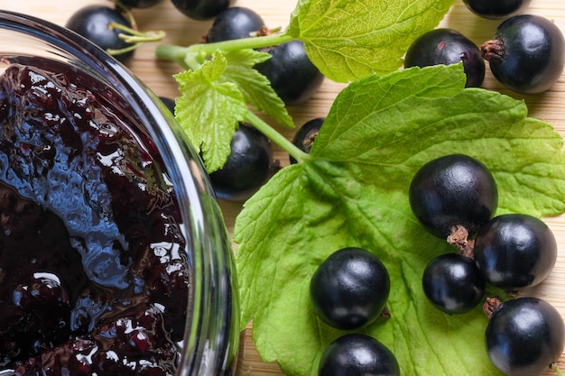 Ripe black currant berries on the kitchen table next to a bowl
of currant jam close-up macro photography