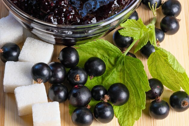 スグリジャムと角砂糖のクローズアップマクロ写真のボウルの横にあるキッチンテーブルの熟した黒スグリの果実