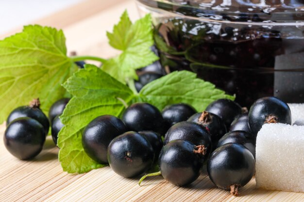 Ripe black currant berries on the kitchen table next to a bowl of currant jam and sugar cubes close-up macro photography