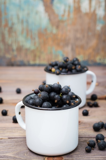 Ripe black currants in metal white mugs on a wooden table