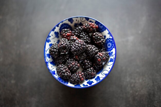 Ripe blackberries in a clay bowl on a light black background.