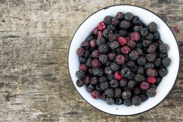 Ripe blackberries in rustic bowl on old wooden background. Top view