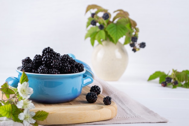 Ripe blackberries with leaves in a blue ceramic bowl on white table