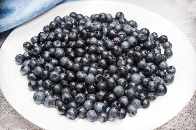Ripe blueberries lie on a white plate on a light background with a blue napkin Summer vitamins Horiz