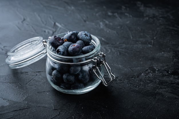 Ripe blueberry in glass jar, on black table.