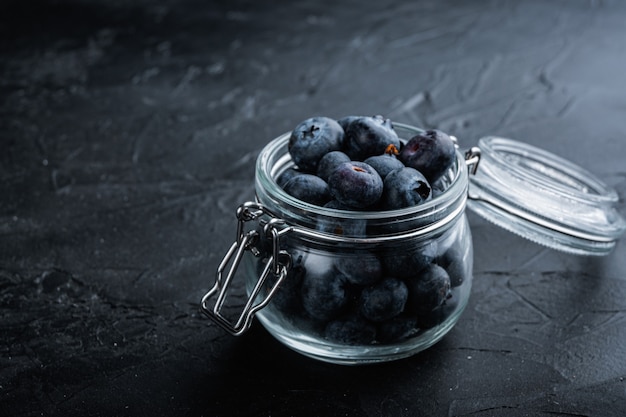 Ripe blueberry in glass jar with space for text, on black background.
