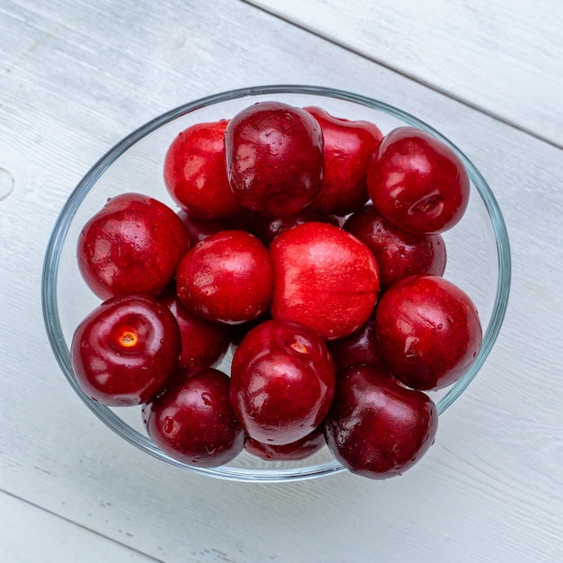 Ripe cherries in a glass bowl on a white wooden background