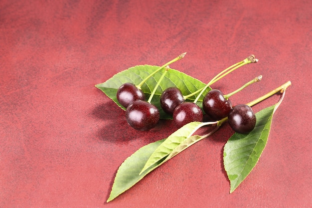 Ripe cherries with leaves on red surface