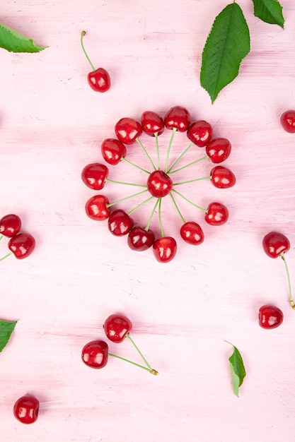 Ripe cherry berries and cherry leaf on pink surface