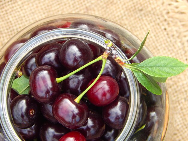 Ripe cherry with leaves in a glass jar, close up