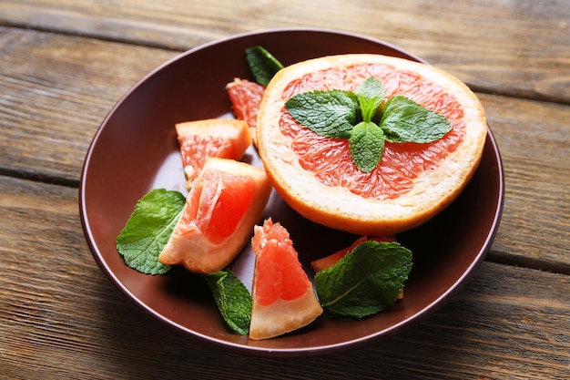 Ripe chopped grapefruit with mint leaves on plate on wooden background