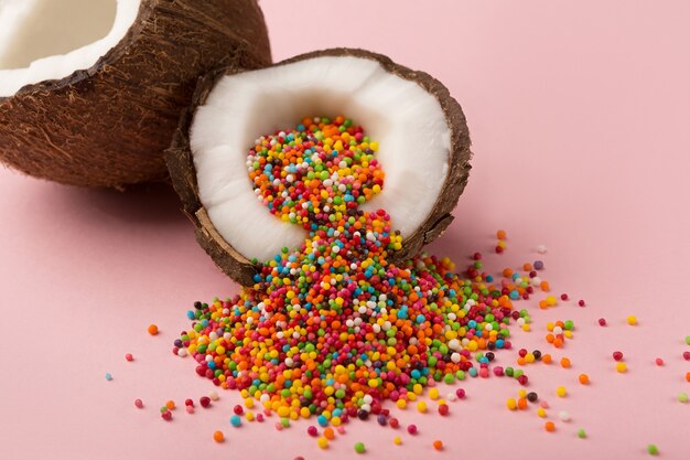 Metà di cocco maturo con zuccherini colorati all'interno su sfondo rosa studio. sfondo creativo, design di biglietti di auguri di pasqua, spazio di copia