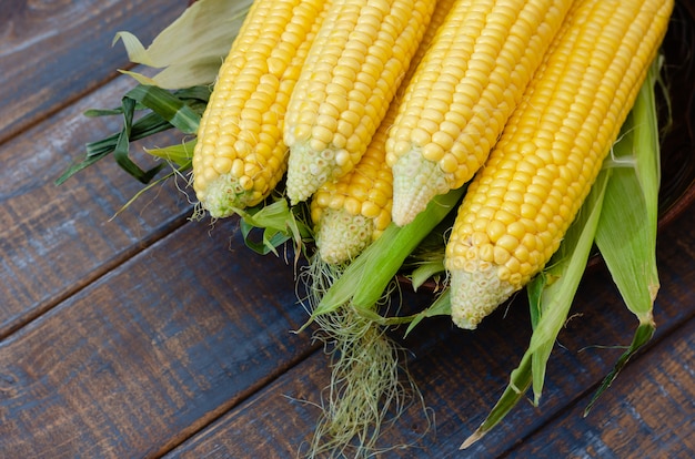 Ripe corn in a clay bowl on a dark brown wooden background.