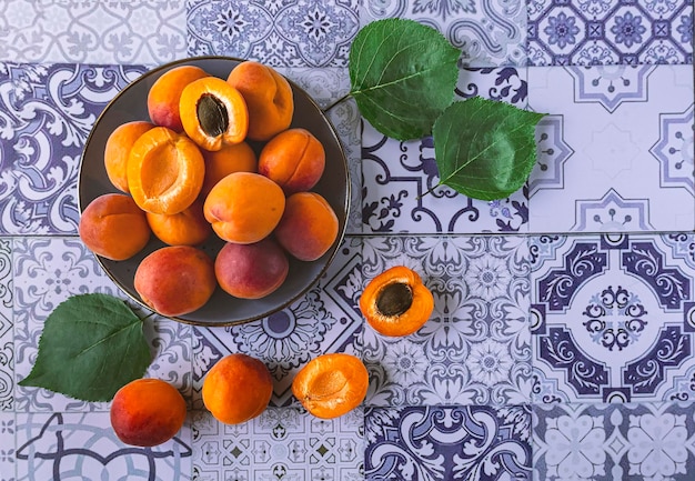 Ripe and cut orange apricots with leaves on a plate on a blue background top view