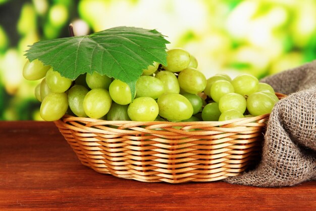 Ripe delicious grapes in wicker basket on table on bright background