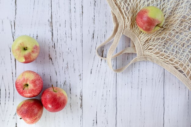 Ripe delicious red apples and a bag on a light background, top view. New summer harvest. The concept of healthy food.