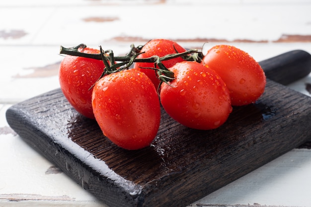 Ripe fresh cherry tomatoes on a branch on a wooden chopping Board. Wooden rustic table. Copy space.