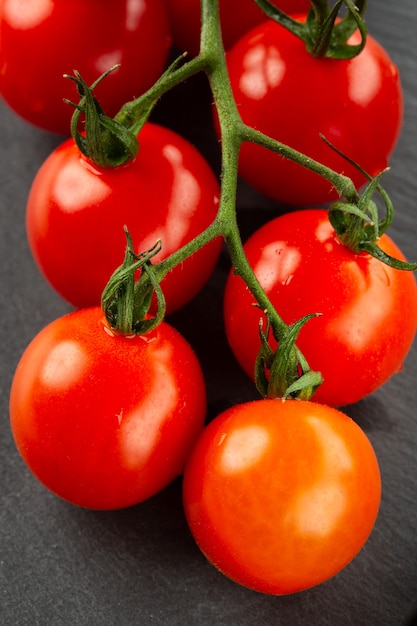 Pomodorini freschi maturi che sembrano gustosi e lucenti mentre vengono posti sulla superficie grigio scuro