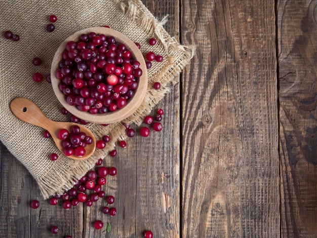 Ripe fresh cranberries in a wooden bowl on a rustic table top.