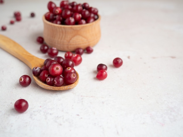 Ripe fresh cranberries in wooden bowl and wooden spoon on concrete table top with copy space