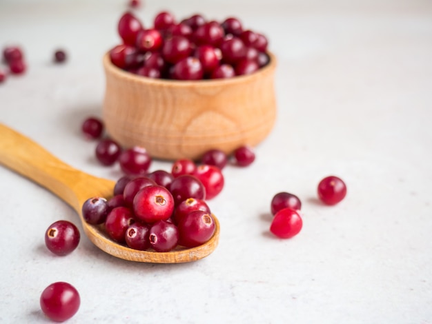 Ripe fresh cranberries in wooden bowl and wooden spoon on concrete table top with copy space