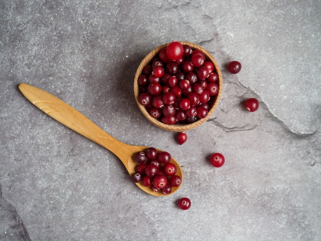 ripe fresh cranberries in wooden bowl and wooden spoon on concrete table top with copy space