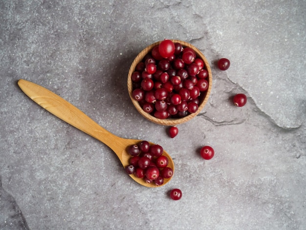 Ripe fresh cranberries in wooden bowl and wooden spoon on concrete table top with copy space