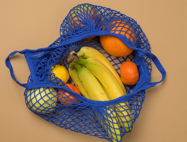 Ripe fresh fruits in a textile string bag on a brown background, top view