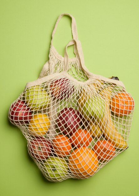 Photo ripe fresh fruits in a textile string bag on a green background, top view