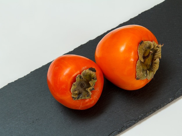 Ripe fresh persimmon fruits on stone cutting board.