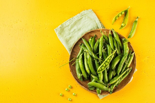 Ripe fresh young green peas in a wooden plate on a yellow background copy space