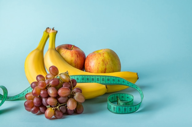 Ripe fruits and measuring tape on a blue space. The concept of diet and proper nutrition.