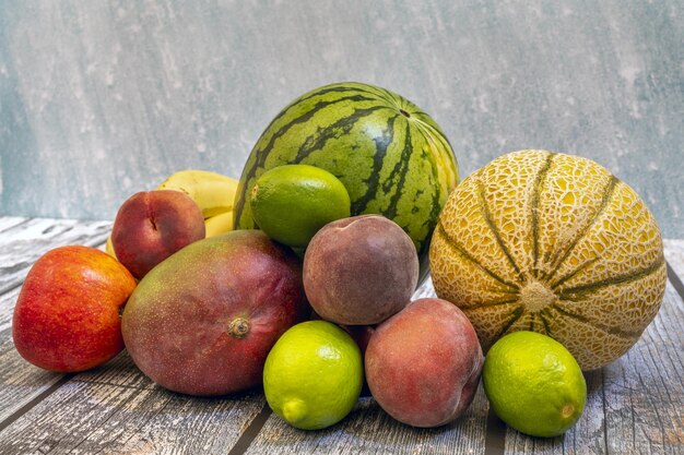 Спелые фрукты, готовые к употреблению в летний день, красные персики, зеленые лаймы, дыни и арбузы, африканские манго на деревянном столе