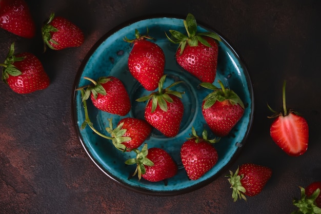 Ripe garden strawberry in blue plate on dark stone table