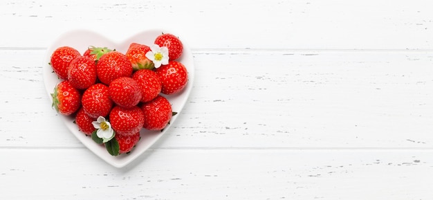 Ripe garden strawberry on heart shaped plate on wooden table Top view flat lay with copy space